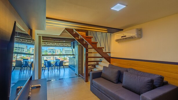 A living room with a sofa, a TV, a staircase, and a view of the outside. - Tangaroa Flats em PG por Carpediem (Ipojuca)