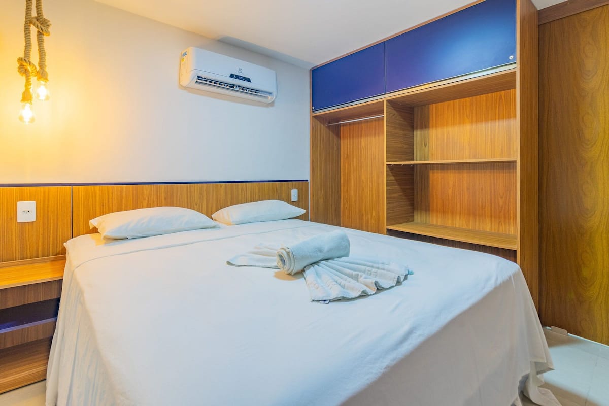 A hotel room with a bed, a wardrobe, and a wall-mounted air conditioner.