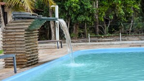 Una piscina con caída de agua, rodeada de un muro de piedra y vegetación.