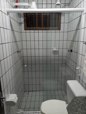 A small, tiled bathroom with a toilet, a shower area, and a window above the shower. - Pousada Orla Náutica (Barreirinhas)