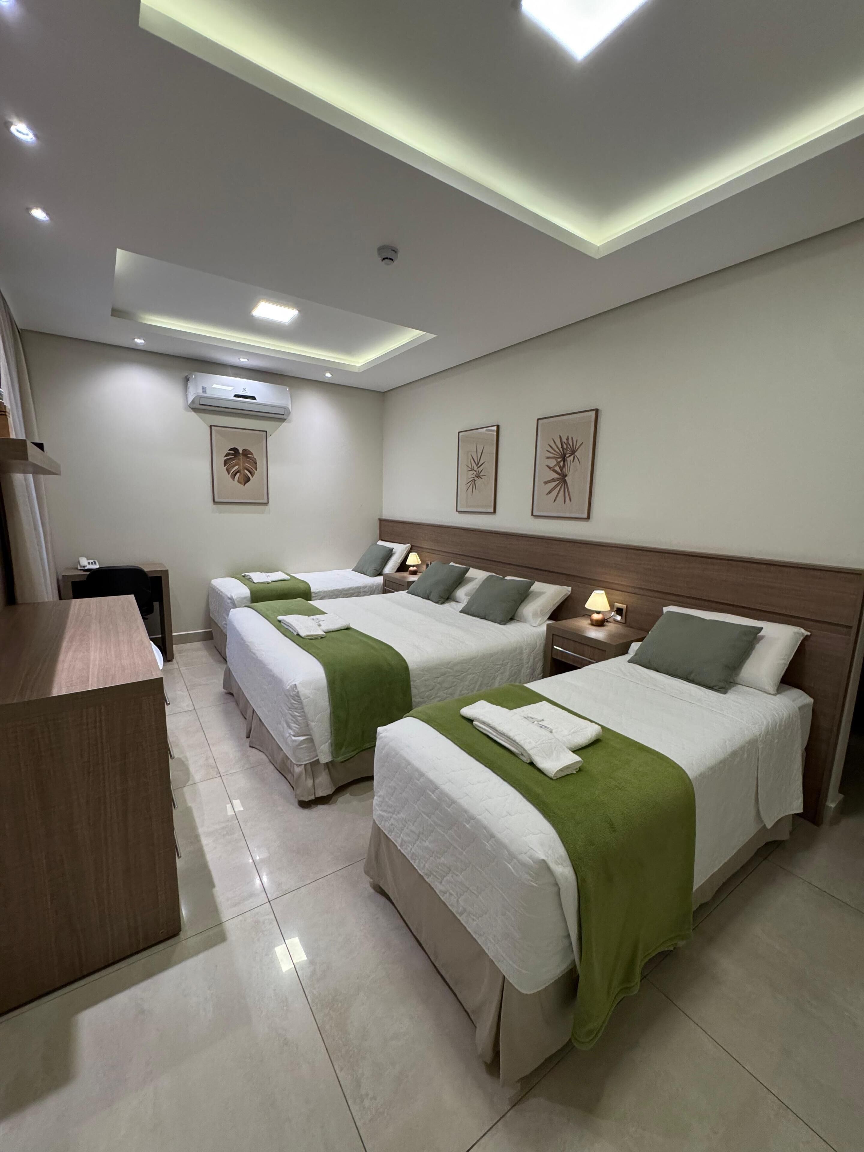 Habitación de hotel con tres camas, un escritorio y una lámpara en el techo.