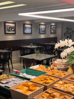 Un restaurante con mesas y sillas, cuadros en la pared y un bufé con diversas opciones de comida.