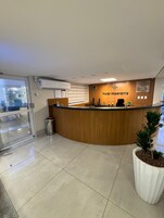 Mostrador de recepción de hotel con detalles de madera, un reloj y un cartel que enumera los tipos de habitaciones.