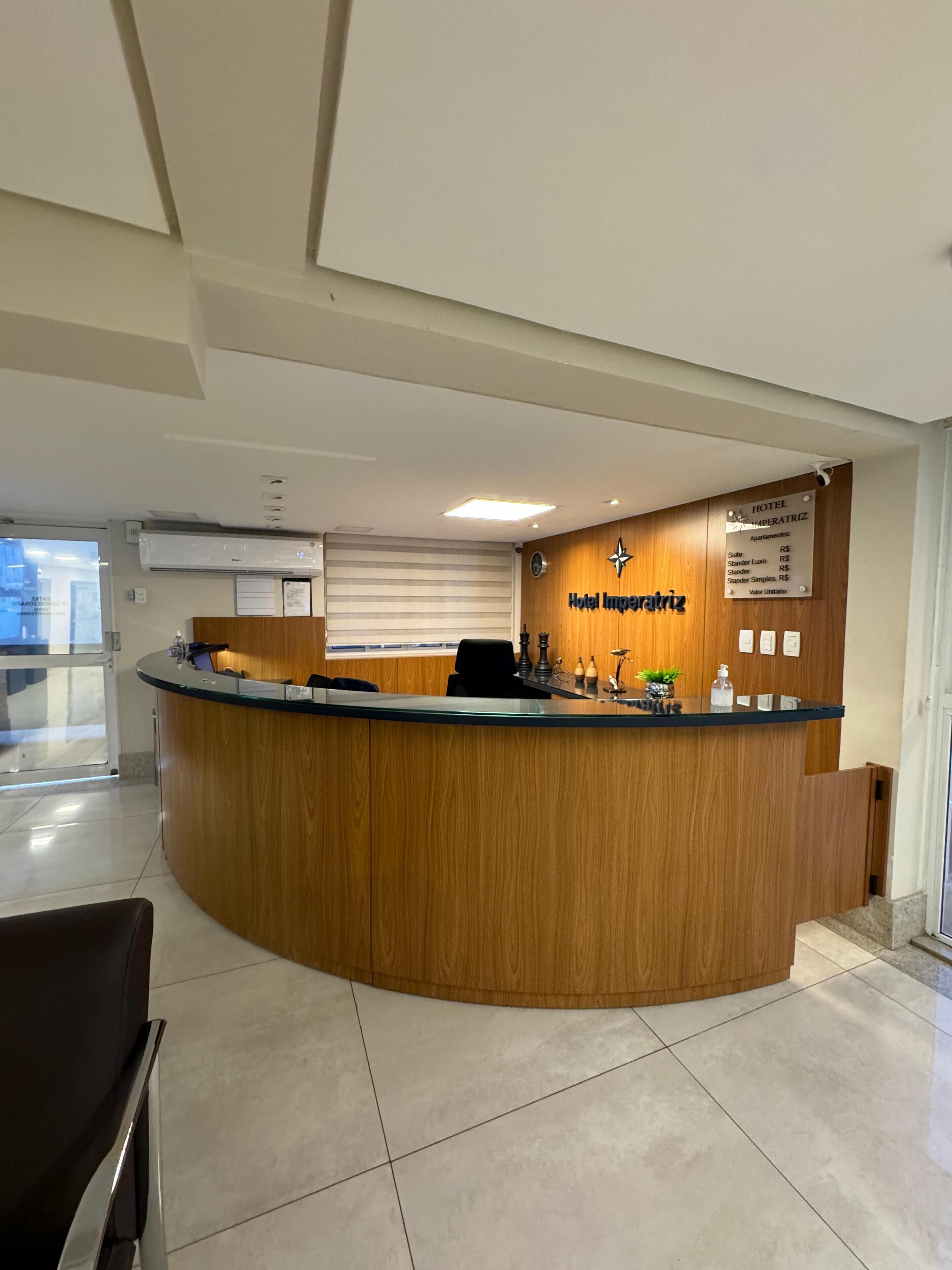 A hotel reception desk with a wooden finish, a sign above indicating the hotel name, and a list of room types and prices.