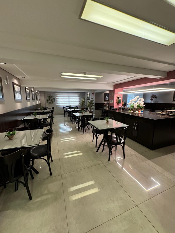 Un'area pranzo moderna con diversi tavoli e sedie, un angolo cottura con un bancone ed elettrodomestici, e quadri appesi alle pareti.