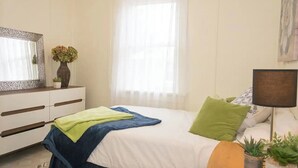 A bedroom with a bed, a dresser, a mirror, a window with sheer curtains, and a lamp. - Smooth Rock Falls Countryside Comfortable and Stunning 4 bedroom Spacious House (Smooth Rock Falls)