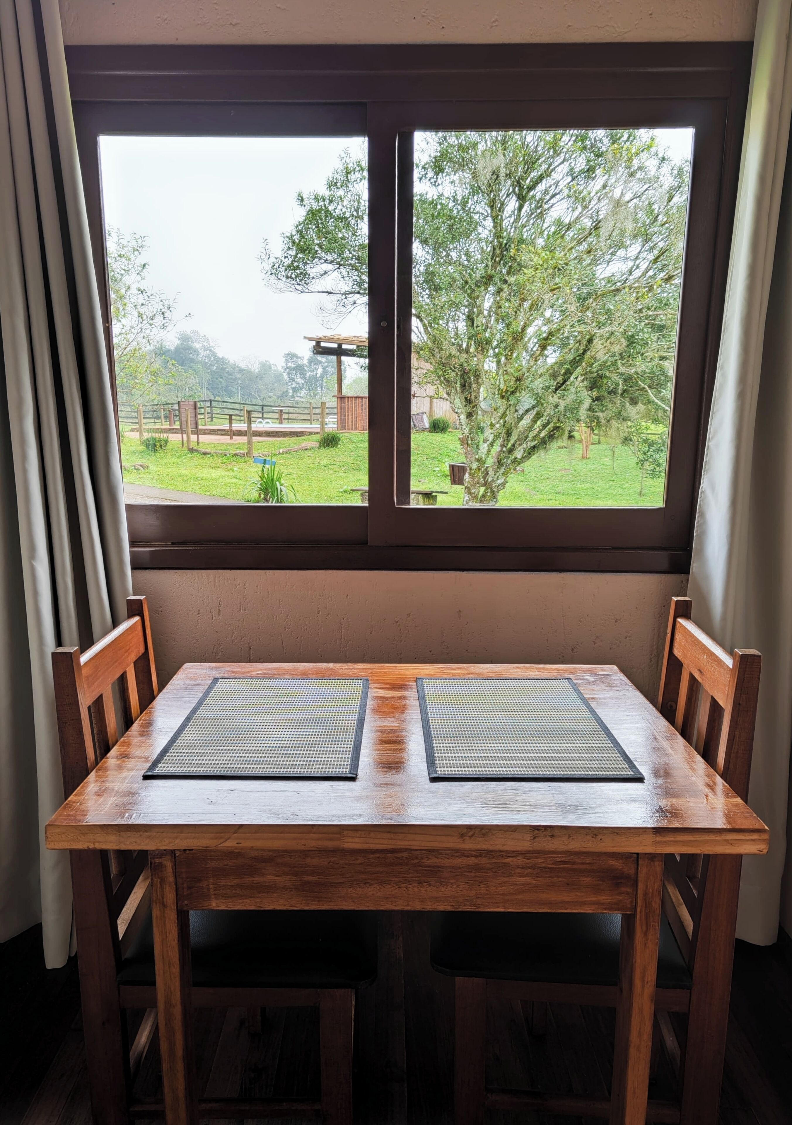 Una mesa de madera con dos caminos de mesa negros, una ventana que da a un jardín y cortinas a cada lado.