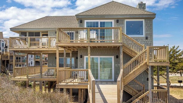 A two-story beachfront house with a wooden deck, a glass door entrance, and a staircase leading to the upper level. - Lawrence, Ships Watch Community in Duck, NC (Duck)