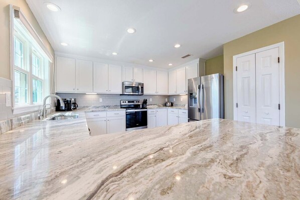 A spacious kitchen with white cabinets, a stainless steel refrigerator, and a marble countertop.