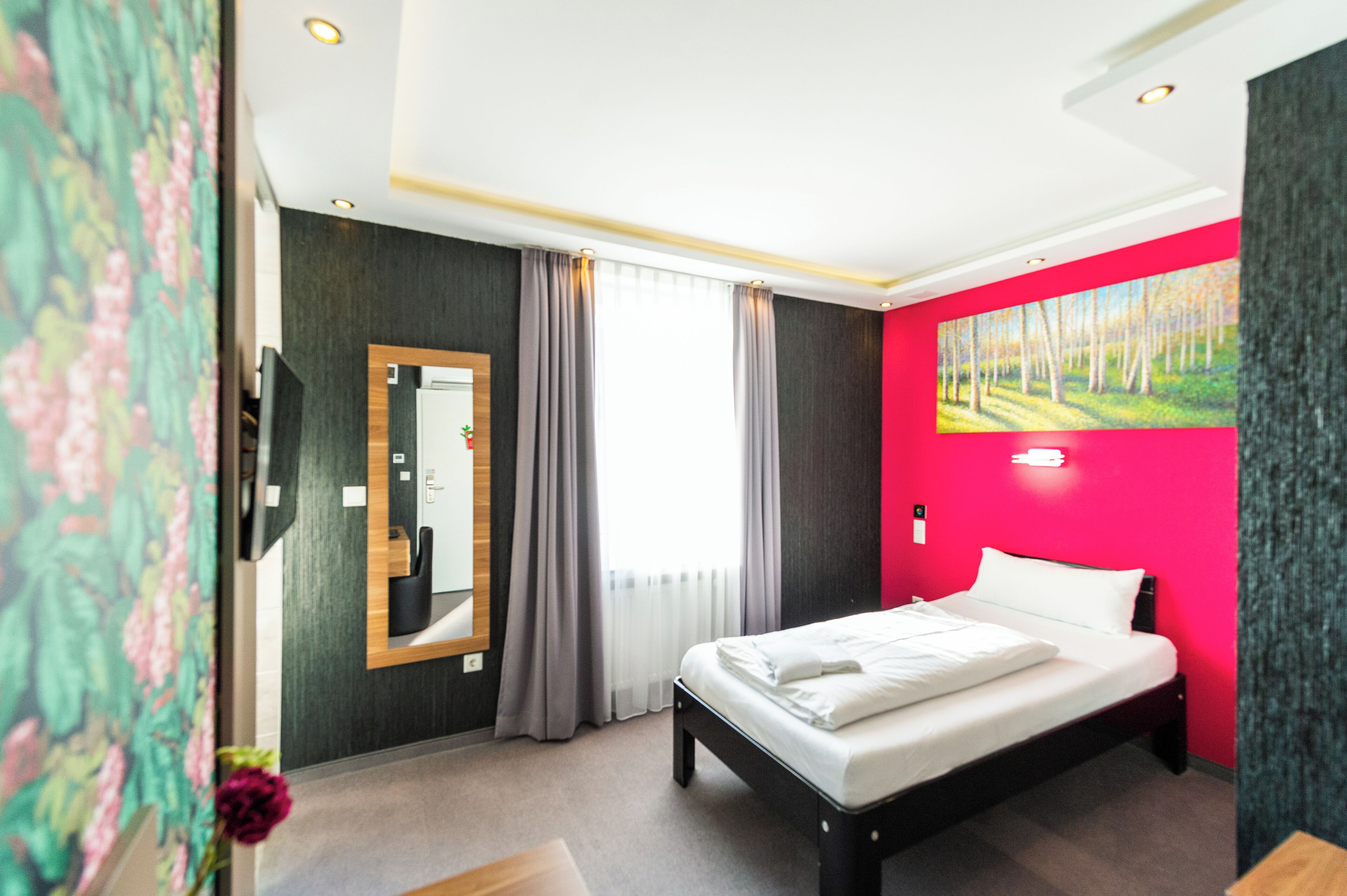 Ein Hotelzimmer mit Bett, Spiegel, einem Fenster mit Vorhängen und einem Bild an der Wand.