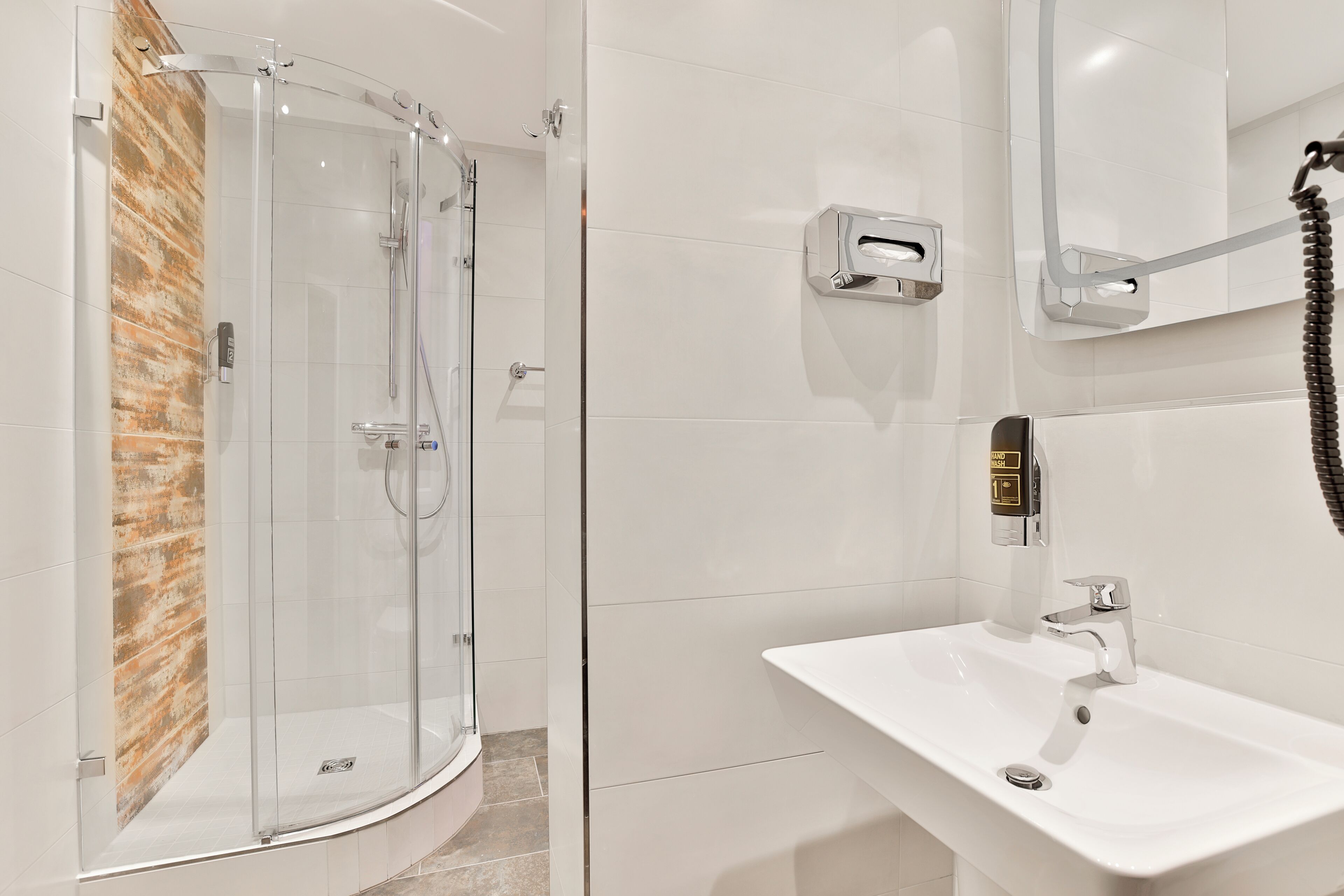A modern bathroom with a glass-enclosed shower, a white sink, and a towel dispenser.