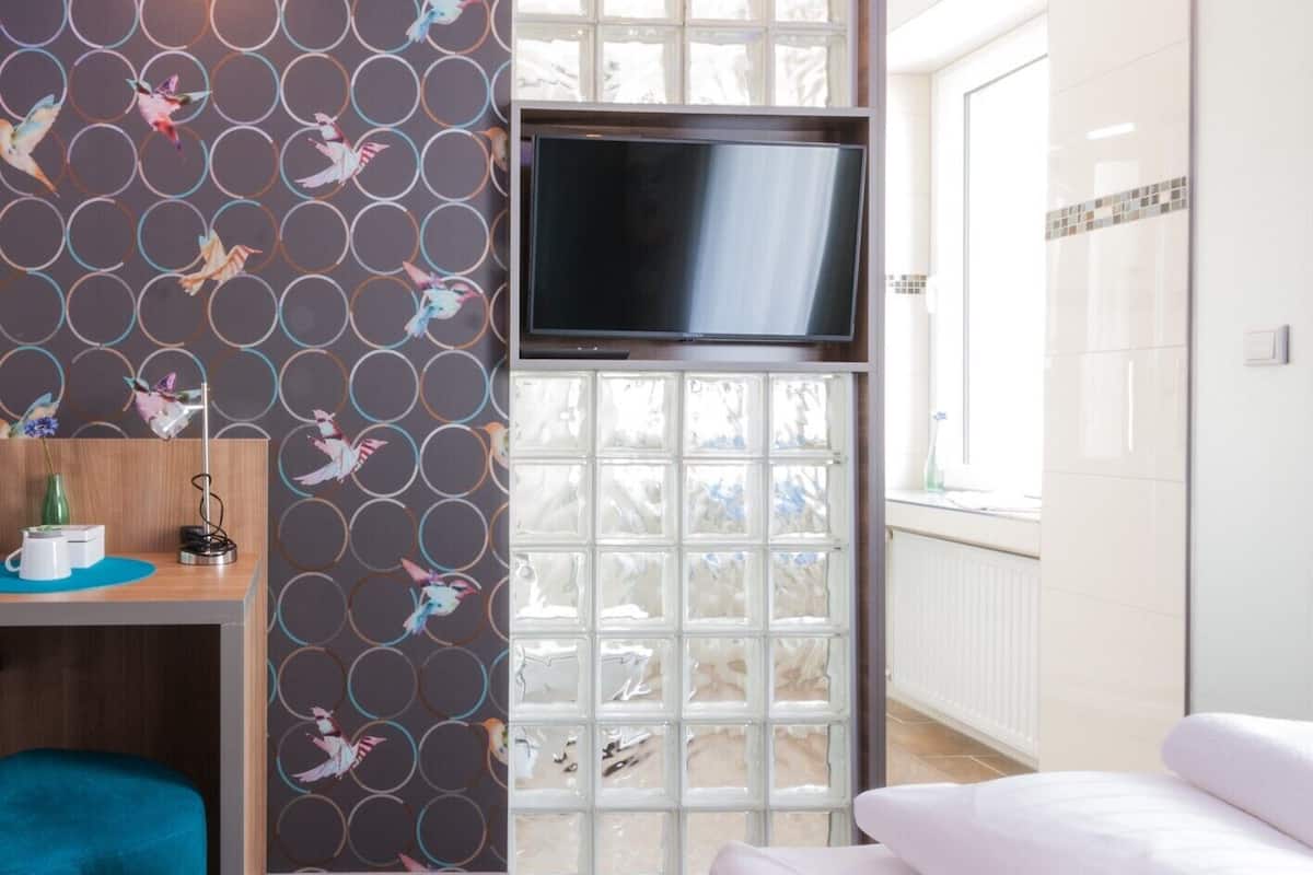 A hotel room with a TV mounted on a wall, a window with a view of the outside, and a bed with white bedding.