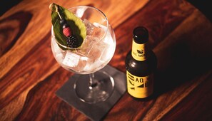 Een cocktailglas met ijs en fruit, een fles drank, en een onderzetter op een houten tafel.