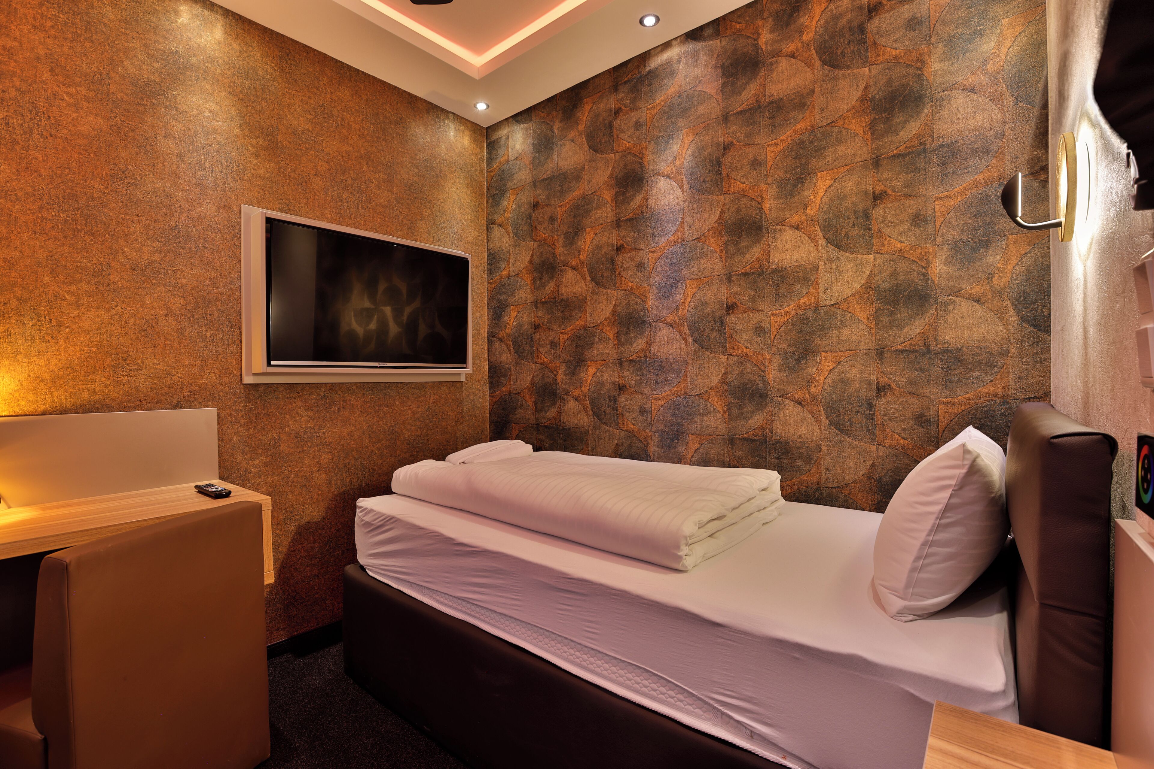 A hotel room with a bed, a desk, and a TV mounted on the wall.