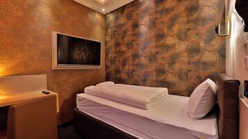 A hotel room with a bed, a desk, and a TV mounted on the wall.