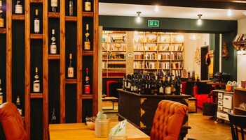 A bar area with wooden shelves of bottles, a seating area with leather chairs, and a bookshelf filled with books.