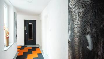A hallway with a black and orange chevron-patterned floor, a door at the end, and a large elephant sculpture on the right wall.