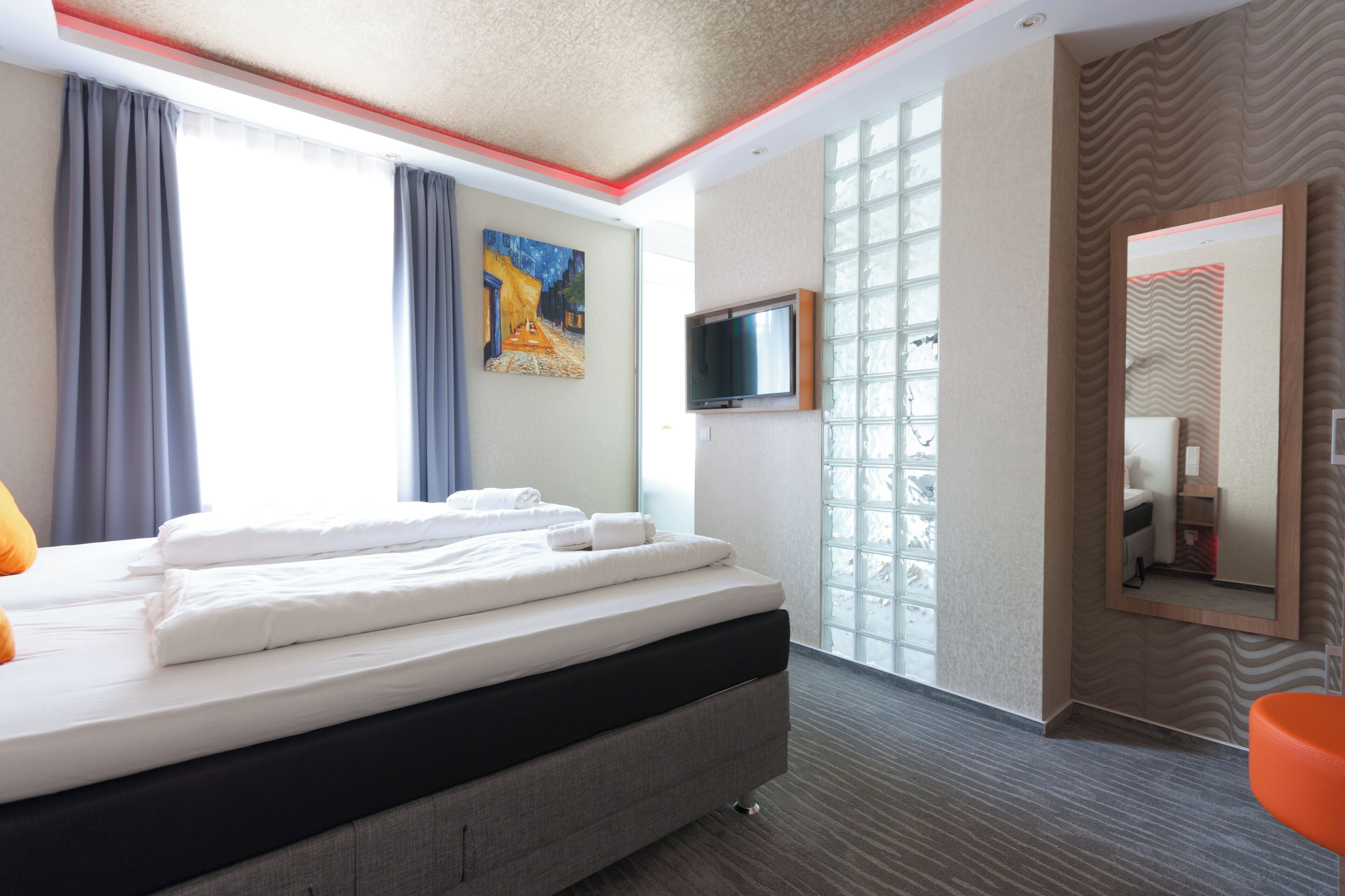 A hotel room with a bed, a TV, a painting, and a bathroom mirror.