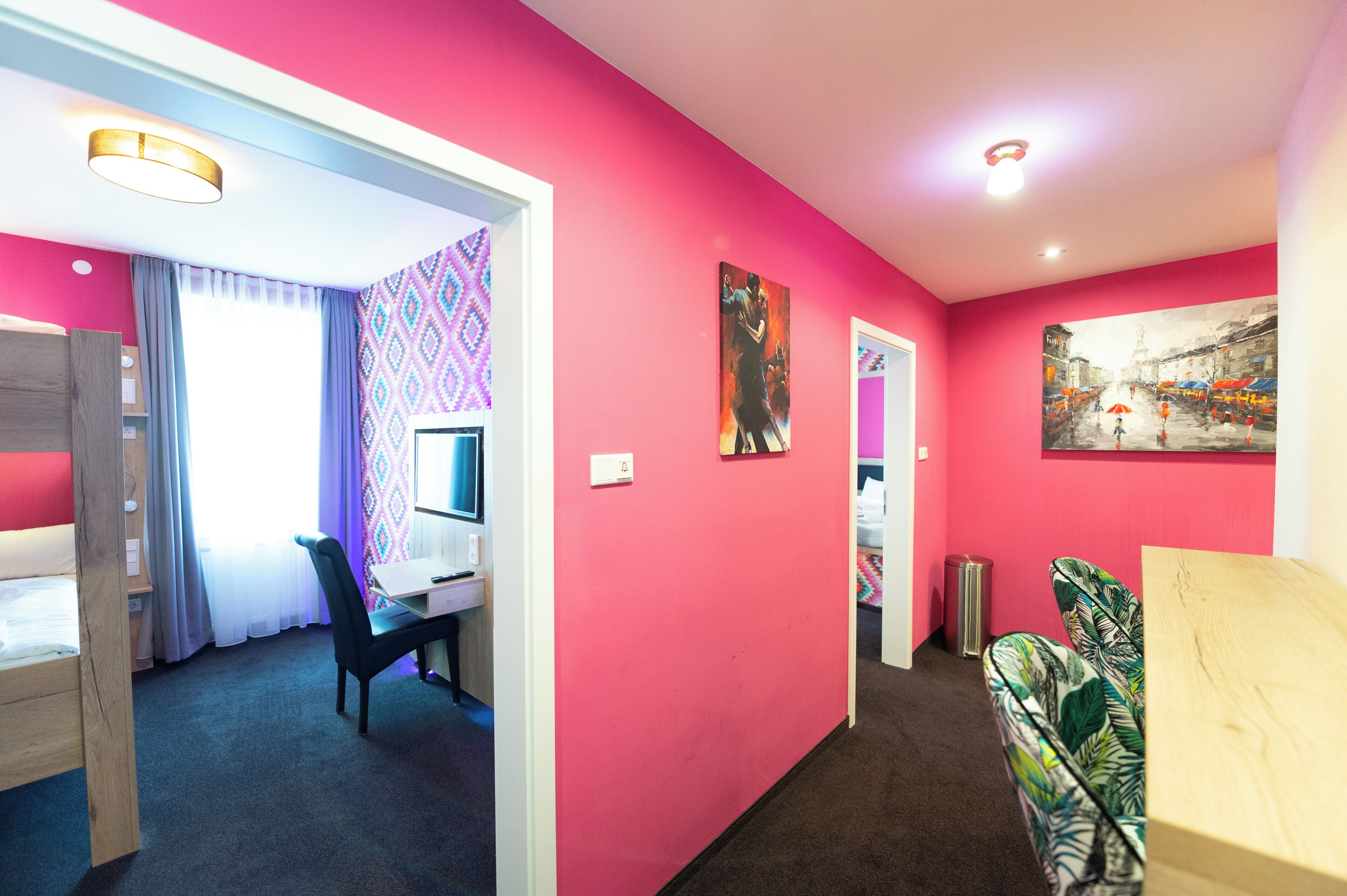 Une pièce avec un mur rose, un bureau avec un ordinateur, une chaise et un lit.