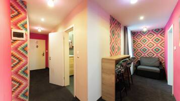 A hallway leading to a room with a patterned wall, a wooden desk, and a gray sofa.