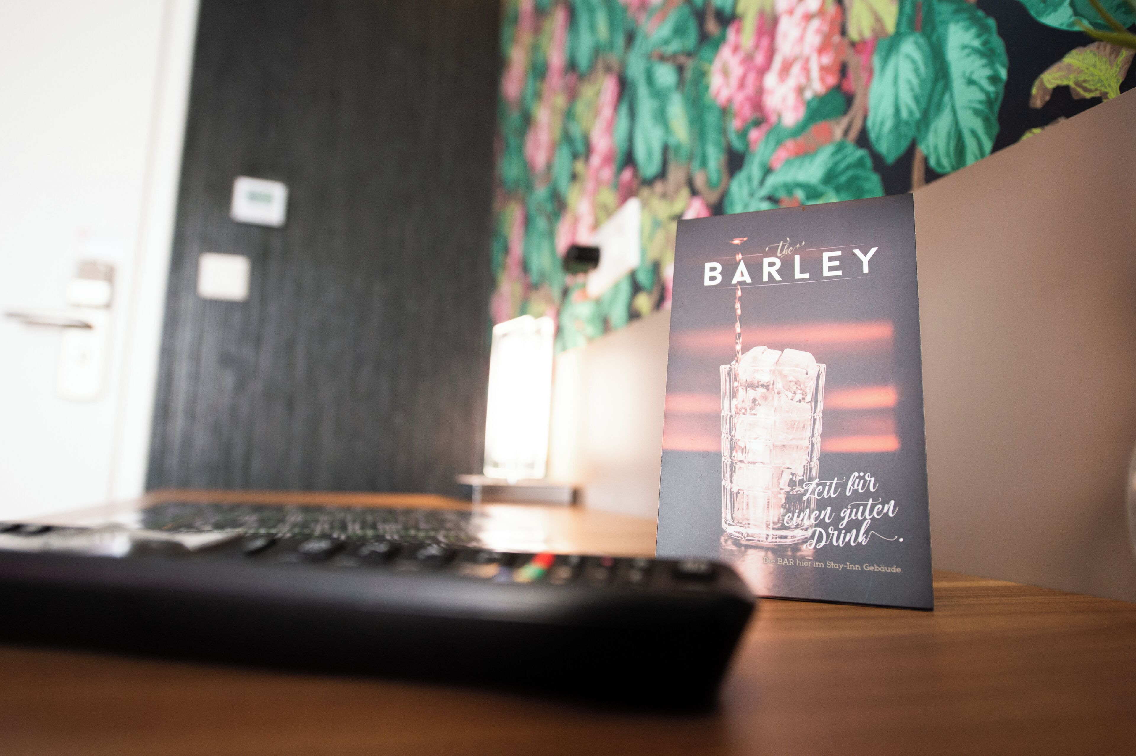 A remote control on a wooden surface with a Barley branded card and a candle in the background.