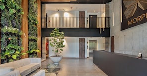 Una hall moderna con una reception, un'ampia pianta in vaso, un'area salotto e un giardino verticale.