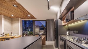 A modern kitchen with a central island, built-in appliances, and a view of the city at dusk. - Luxe apt in Poblado/AC/BBQ - Morph 1002 (Medellín)