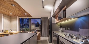 A modern kitchen with a central island, built-in appliances, and a view of the city at dusk. - Luxe apt in Poblado/AC/BBQ - Morph 1002 (Medellín)