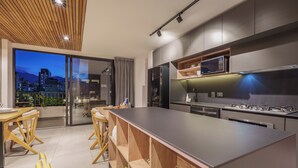 A modern kitchen with a large island, built-in appliances, and a view of the city at dusk. - Luxe apt in Poblado/AC/BBQ - Morph 1002 (Medellín)