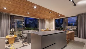 A modern kitchen with a central island, a dining area with a sofa, and large windows offering a city view. - Luxe apt in Poblado/AC/BBQ - Morph 1002 (Medellín)