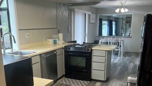 A modern kitchen with a stove, microwave, and sink. There is a dining area with a table and chairs. - Tranquil Riverfront Retreat Near Tillamook's Best
 (Tillamook)