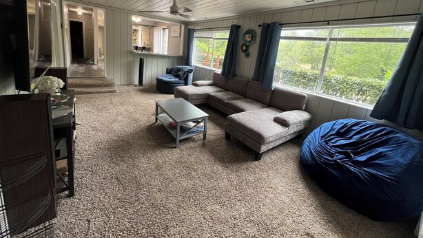 A living room with a sofa, a bean bag, a coffee table, and a TV. There is a window with curtains and a view of greenery outside. - Tranquil Riverfront Retreat Near Tillamook's Best
 (Tillamook)