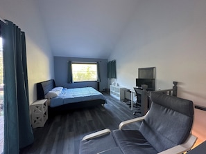 Ett hotellrum med en säng, ett skrivbord med en stol, en tv och ett fönster med gardiner.