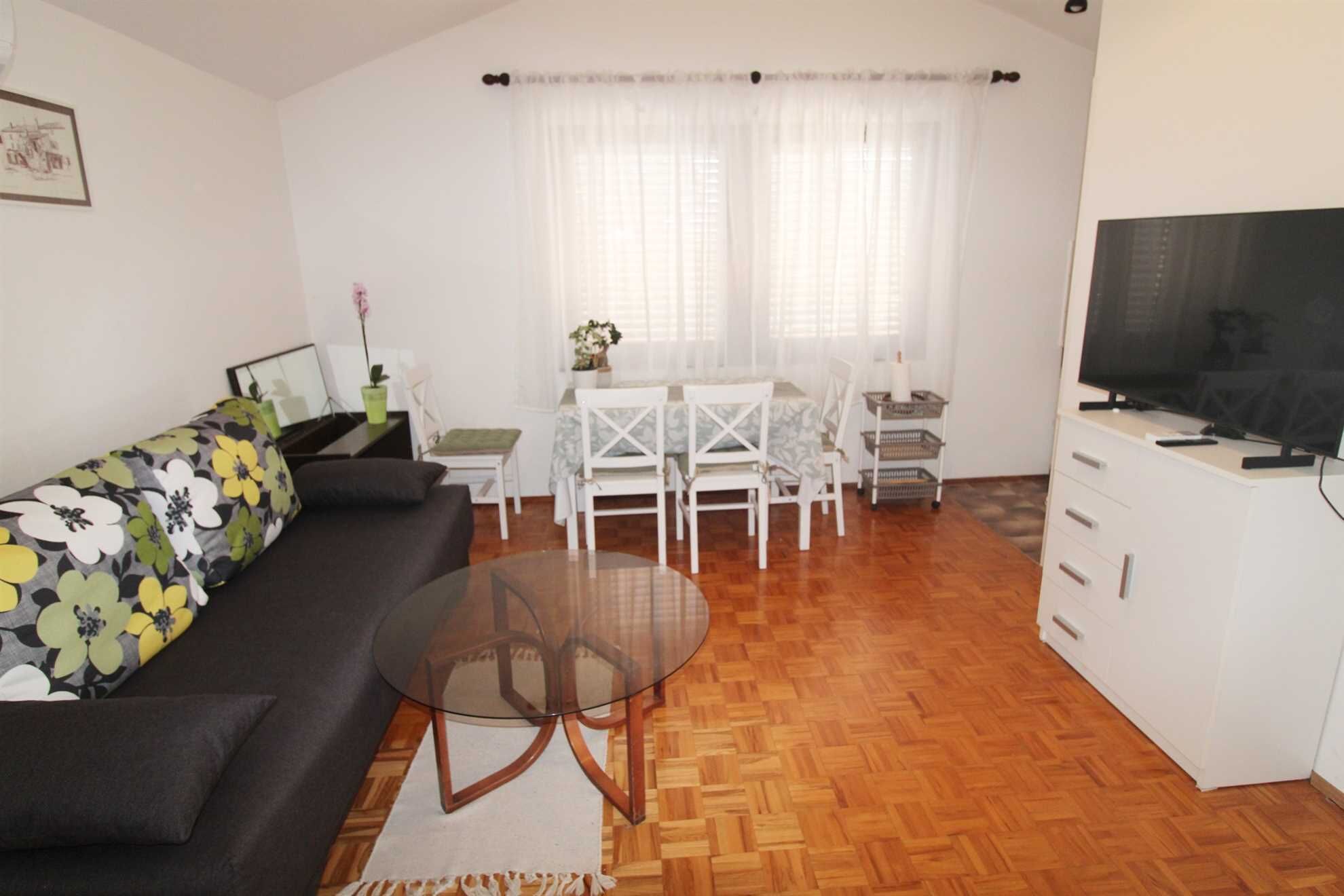 A compact living space with a sofa, a glass coffee table, a dining table with chairs, a TV, and a small cabinet.