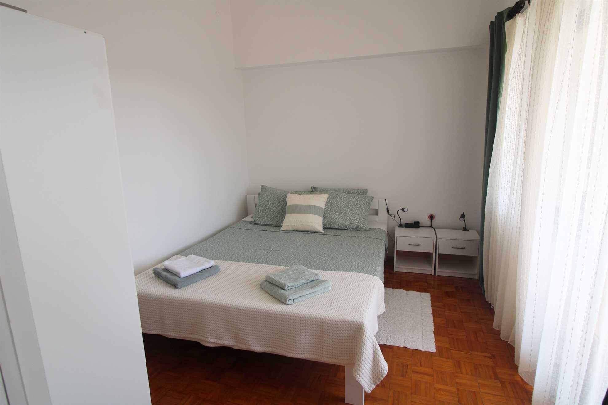 A bedroom with a bed, bedside tables, a desk, and a window with curtains.