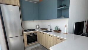 Moderni keittiö, jossa on ruostumattomasta teräksestä valmistettu jääkaappi, puukaapit, kaasuliesi ja sisäänrakennettu uuni.