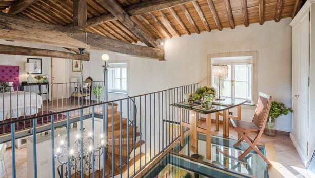 Ein geräumiges Interieur mit Holzbalkendecke, einer Treppe, einem Essbereich mit Glastisch und Blick ins Freie.