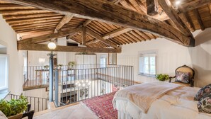 Ein Schlafzimmer mit einem großen Bett, Holzboden, einem Balkon mit Geländer und Blick ins Innere.