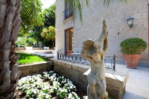 A courtyard with a stone statue, white flowers, a palm tree, and a building with a balcony. - Villa Ebe in Sorrento (Sorrento)