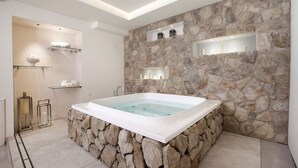 A modern bathroom with a stone wall, a bathtub, and shelves with toiletries. - Villa Ebe in Sorrento (Sorrento)