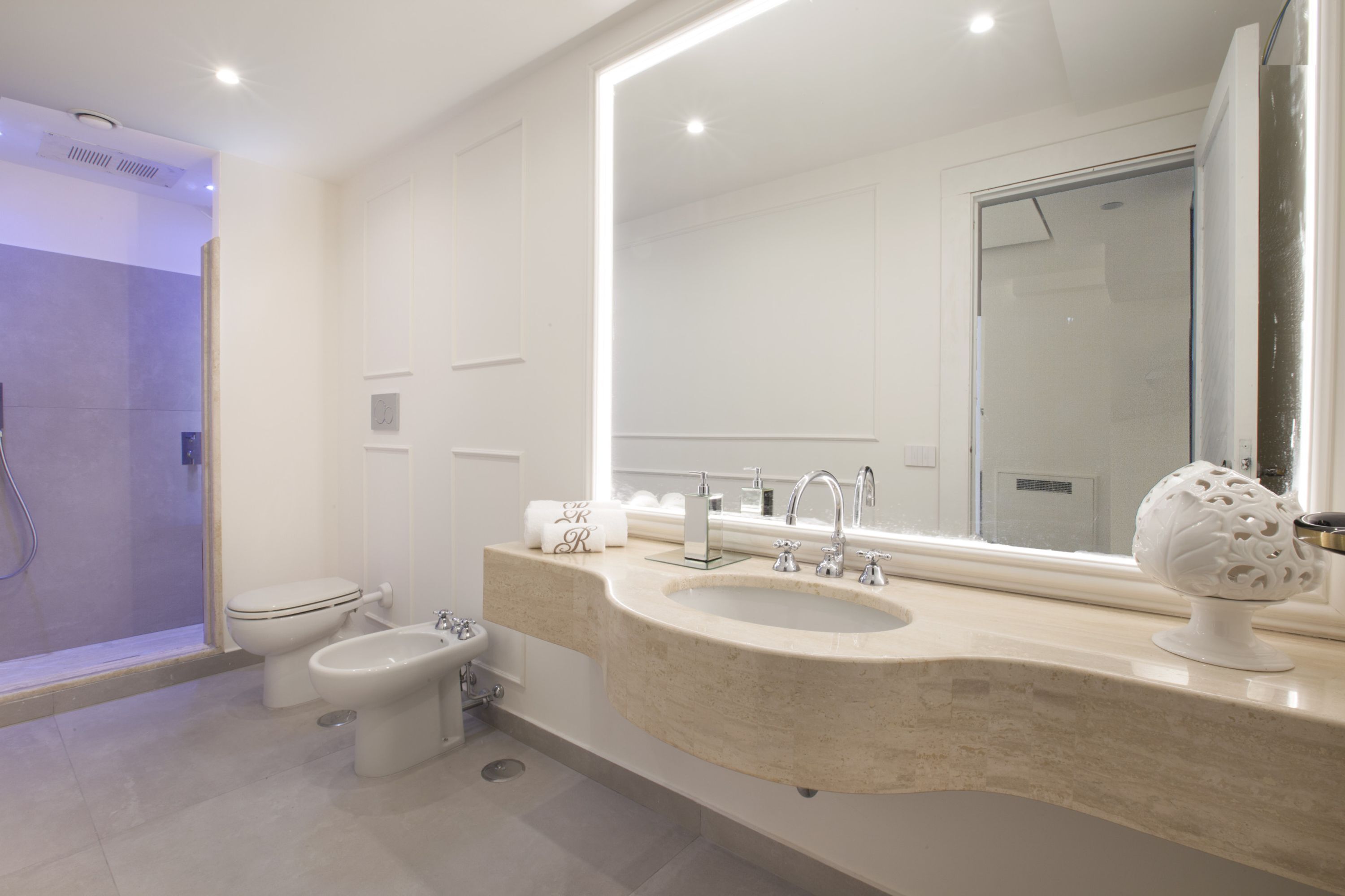 A modern bathroom with a shower, toilet, bidet, sink, and a large mirror.