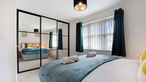 Een moderne slaapkamer met een groot bed, een spiegel, een raam met gordijnen en een hanglamp.