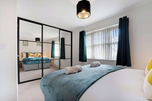 Un dormitorio moderno con una cama grande, un espejo, una ventana con cortinas y una lámpara colgante.