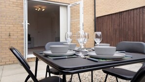 Een terras met een tafel voor vier personen, stoelen en een schuifdeur naar een kamer.