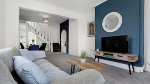 Una sala de estar moderna con un sofá gris, un mueble para televisión y una escalera que lleva a otra habitación.