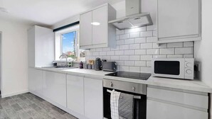Una cocina moderna con armarios blancos, una ventana, un microondas y una tetera.