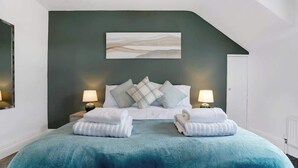 Un dormitorio con una cama, almohadas, dos lámparas de noche, un cuadro en la pared y una puerta.