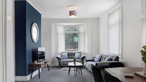 Una sala de estar moderna con un sofá gris, una mesa de centro redonda y un televisor sobre un mueble.
