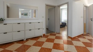 Un couloir avec un sol à carreaux, une armoire blanche avec des tiroirs, un miroir et une porte donnant sur une autre pièce.