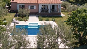 Une maison à deux étages avec une piscine, entourée de verdure et de collines.